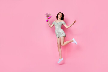 Full length photo of cheerful funny girl dressed off shoulders outfit jumping holding flowers empty space isolated pink color background