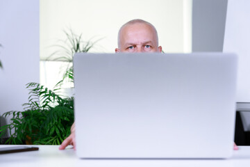 a gray-haired man with a very short haircut sits at a laptop and stares intently at the screen....