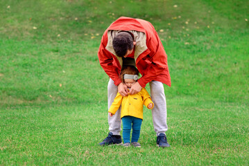 Father buttoning jacket of toddler girl on walk. Dad and baby daughter walking together in park in autumn day. Father leaned to child. Parental care concept