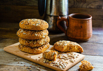 Oatmeal homemade cookies with grains on a wooden board, on the kitchen table and homemade coffee in a clay mug.