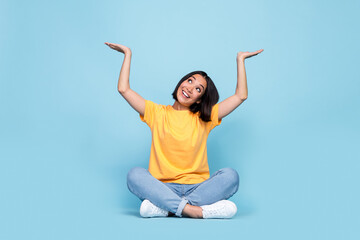 Full body size photo of young japanese pretty girl bob brunette hair interested look up hold palms object advert empty space isolated on blue color background