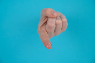 A woman's hand sticks out through a blue paper background and holds a contact lens.