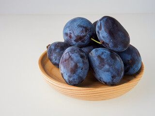 Black plums on wood background. Pile of black plums on a white serving plate. close up