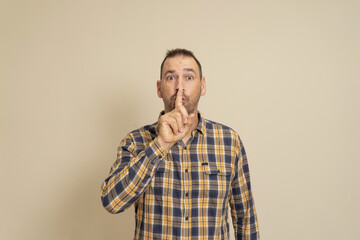 Serious good looking male, keeps fore finger on lips, tries to keep conspiracy, looks aside, says: Shh, make silence please. Isolated shot of attractive man shows silence sign.