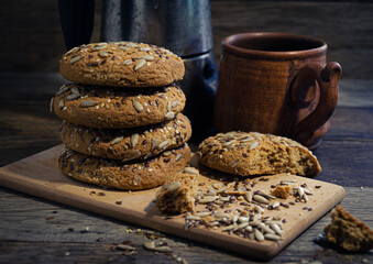 Oatmeal homemade cookies with grains on a wooden board, on the kitchen table and homemade coffee in a clay mug.