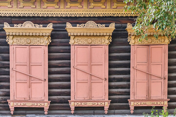 Old wooden painted windows. Carved yellow architraves, closed coral shutters. Ulan-Ude,Russia. - obrazy, fototapety, plakaty
