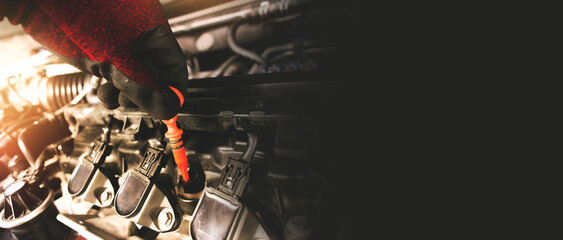 A mechanic is pulling the orange dipstick to check the oil level of the combustion engine in the...