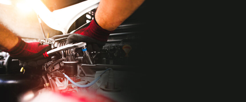 The red gloved hand of the auto mechanic is fastening the bolt with the socket wrench to fix the vehicle engine ,  horizontal banner copy space on black background