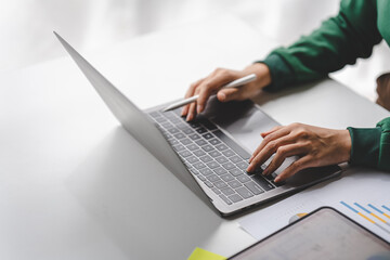 Close-up of young woman's hand typing on laptop computer keyboard and surfing internet on desk,...