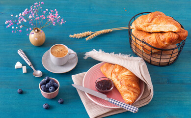 Tasty breakfast with croissants, fresh blueberries, jam and cup of coffee. Blue wooden table, high...