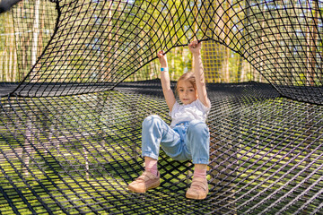 child having fun in net tunnel in playground or amusement park.