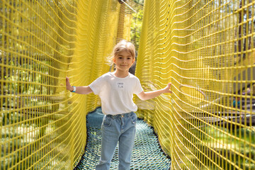 Girl crawls on a net in an obstacle course. Netting amusement park.