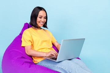 Photo of lovely cute pretty girl wear yellow t-shirt sit on purple bean bag chair writing code in...