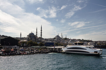 View of a ferry boat, historical mosques in Eminonu area and many people in Istanbul. It is a sunny summer day.