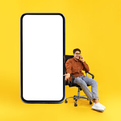 Man Talking On Cellphone Near Large Smartphone Sitting, Yellow Background