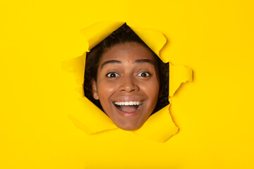 Excited African Woman Looking Through Hole In Torn Yellow Paper