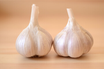 Close-up and front view of two organic garlic heads on a wooden table with a wooden background.