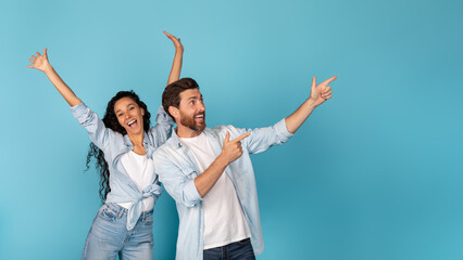 Happy excited young european man and arabic lady rejoice to success, showing fingers to empty space