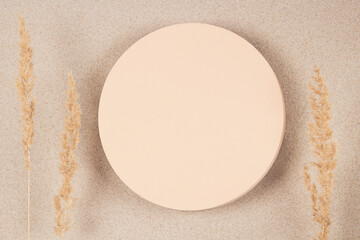 Round beige platform podium stand and dry bent plant on white beach sand background. Minimal creative composition background for cosmetics or products presentation. Top view