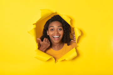 Excited Black Female Looking Through Hole In Paper, Yellow Background