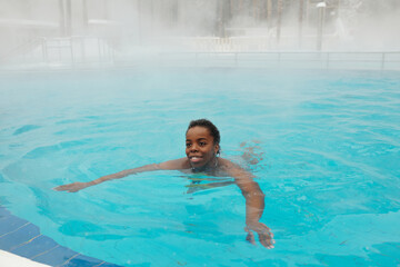 Joyful young African American woman swimming in hot spring pool on winter day, copy space