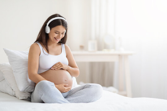 Happy smiling young pregnant woman listening to music in headphones - Powered by Adobe