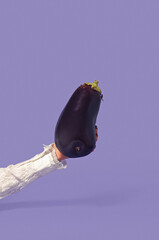 Simple minimal creative concept. An idea with vegetables. A female hand in a white lace shirt holds a fresh and raw dark purple blue eggplant. A veggie idea on the pastel background of Very Peri.