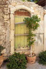 Fototapeta na wymiar Old natural stone wall with shabby wooden door and potted tree 