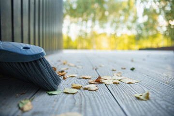 Autumn leaves on the wooden planks of the terrace and a cleaning brush. Close-up.