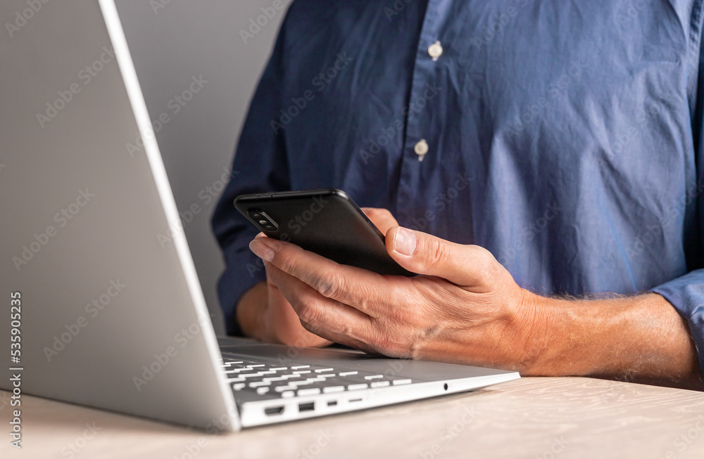 Poster man sitting at table with laptop and holding phone. businessman using smartphone for work or leisure