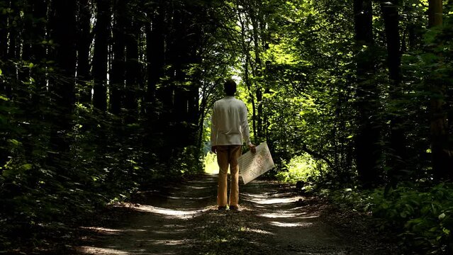Young man artist walking in the green summer forest and holding drawing with numbers in hand. Pavel, i in forest. Date of shooting day 23 July 2022 year, MSK time. Video was filmed in Russia.
