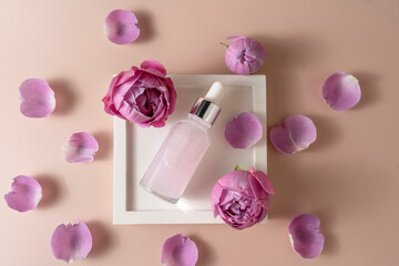 A face serum or essential oil in a pink dropper bottle lying on a white ceramic tray with rose petals around it