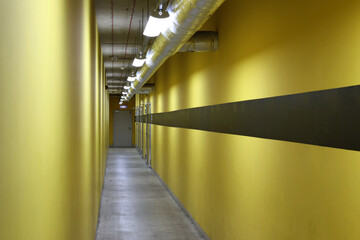 Żółty, długi korytarz z lampami na suficie. Zaplecza.