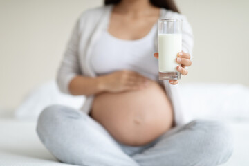 Glass of milk in pregnant woman hand, blurred background