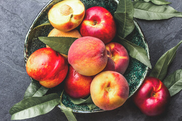 Fresh ripe peach with peach tree leaves in green bowl, top view