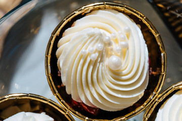 Closeup of cupcakes with cherries in golden cups. Topped with white cream.