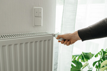 A man regulates the temperature on the radiator at home. Rising prices for heating in households. The concept of the energy crisis in Europe