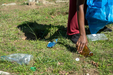 Young woman cleaning up plastics from field. Collecting garbage in a plastic bag