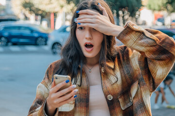 girl in the street looking at the mobile phone surprised or scared reacting excited