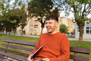 Fototapeta premium A young businessman outdoors in park sitting with his laptop talking on phone enjoying outside 