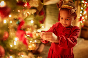 Magical portrait of cute little girl decorating Christmas tree with twinkling lights, copy space