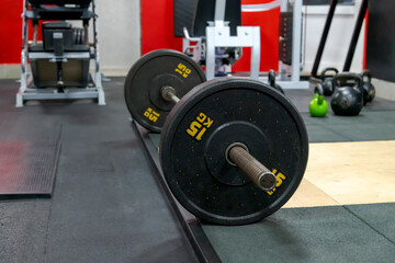 Side view of black barbell with 15 kg plates lying on floor in fitness gym. Selective focus. Sport...