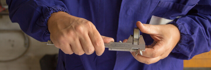 Image of the hands of a mechanic measuring a ball bearing with a caliper. Precision mechanics. Horizontal banner 
