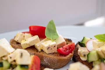 italian bread with greek cheese, tomatoes, cucumbers, radishes and basil and with various spices, on a white plate and a white kitchen table.