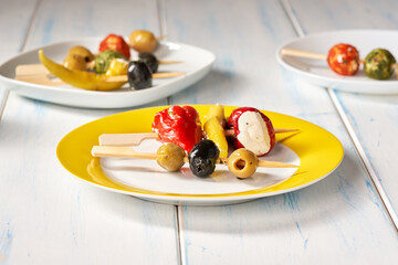 Finger food sticks with olives and stuffed pepperoni on yellow plate.