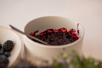 white bowl with blueberries and blackberries and bowl with wild berry jam on white kitchen table and blurred kitchen background, kitchen atmosphere