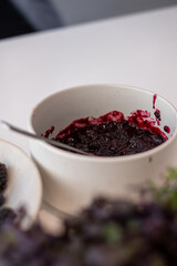 white bowl with blueberries and blackberries and bowl with wild berry jam on white kitchen table and blurred kitchen background, kitchen atmosphere