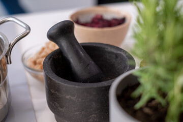 gray pot with growing rosemary on white table, black pestle and blurred kitchen background, kitchen advertising poster, space for your text