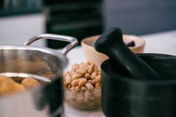 boiled potatoes in a metal pot, beans in a bowl and a pestle on a white kitchen table, with a cozy kitchen background