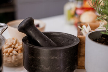 beans in bowl and vegetables in background, pestle on white kitchen table, blurred cozy kitchen background
